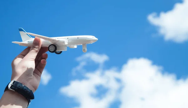 Hand holding airplane model in front of blue sky background. Tra