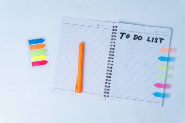 Liste yapmak için el yazısı, turuncu kalem ve beyaz arkaplanda renkli yapışkan notlar bulunan düz spiral bir defter. Planlama, üretkenlik, çalışma ve organizasyon kavramları için mükemmel..