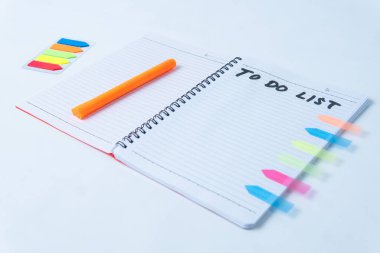 Liste yapmak için el yazısı, turuncu kalem ve beyaz arkaplanda renkli yapışkan notlar bulunan düz spiral bir defter. Planlama, üretkenlik, çalışma ve organizasyon kavramları için mükemmel..