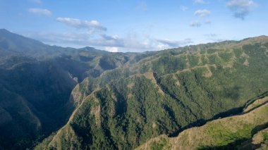 Bereketli yeşil dağların ve açık mavi gökyüzünün altındaki derin vadilerin insansız hava görüntüsü dramatik tepeler, doğal dokular ve el değmemiş tropikal manzaralar sergiliyor..