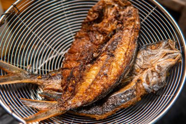 Paslanmaz süzgece yerleştirilmiş kızarmış balığın yakın çekimi. Altın kahverengi doku geleneksel deniz ürünleri mutfağını, Asya sokak yemeklerini ve ev yapımı yemekleri ön plana çıkarıyor. Yemek, beslenme ya da yemek temaları için mükemmel..