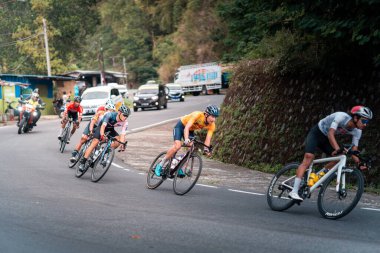 Bajawa, Endonezya - 19 Eylül 2025: Kırmızı formalı bir bisikletçi Tour de NTT yarışında keskin bir virajdan hızla geçer. Uluslararası bisiklet etkinliği sporcuları ve seyircileri Flores 'in manzaralı dağ yollarına çekiyor..