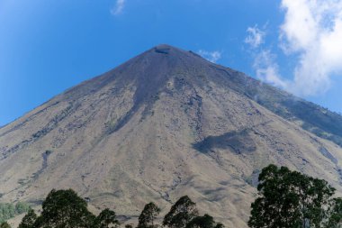 Endonezya, Flores 'te piramit şeklinde bir stratovolcano olan Inerie Dağı' nın manzarası, açık mavi gökyüzü ve ön planda yemyeşil ağaçlar.