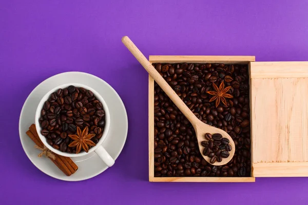 Cup of coffee seeds, cinnamon, anis, wooden box and spoon with coffee on purple background. I love coffee, coffee lover concept. Horizontal orientation, close up.