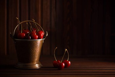 Koyu ahşap arka plan bakır kovanın içinde taze kırmızı kiraz. Yaz,