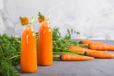 İki şişe taze havuç suyu ve yeşil gri beton zemin üzerine havuç ile. Yatay yönlendirme, yakın çekim.