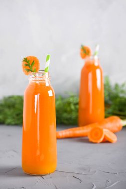 İki şişe taze havuç suyu ile gri beton zemin üzerine yeşil ve düzenlenen adet havuç. Dikey yönlendirme, yakın çekim.