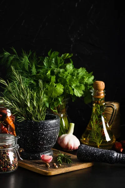 Mermer harç ve dibekler ahşap kesme tahtası, zeytinyağı, sarımsak, otlar siyah arka plan üzerine biberiye ile. Kavramı ile baharat, yemek yemek