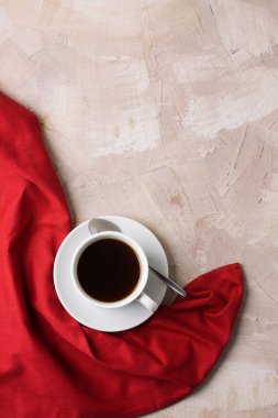 Beyaz fincan kahve ya da çay, bej beton zemin üzerine kırmızı peçete. Dikey yönlendirme, üstten görünüm, düz yatıyordu, kopya alanı, metin için yer.
