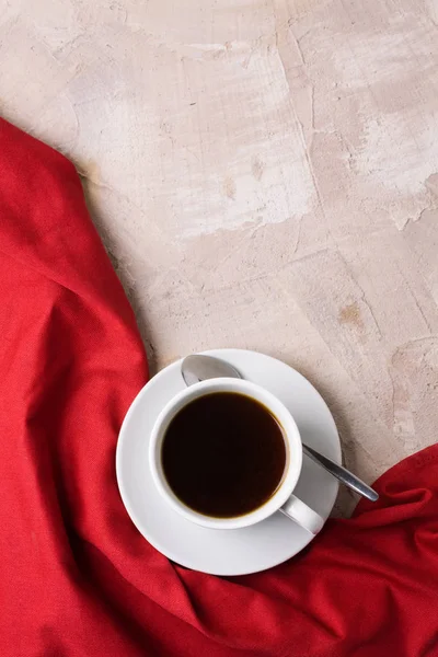Beyaz fincan kahve ya da çay, bej beton zemin üzerine kırmızı peçete. Dikey yönlendirme, üstten görünüm, düz yatıyordu, kopya alanı, metin için yer.