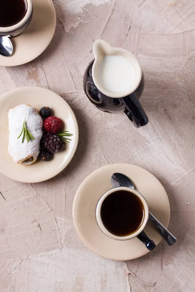 İki mavi metalik Kaşıklar, süt süt ile kahve fincan sürahi, rulo krem, Çilek Böğürtlen, ahududu, siyah frenk üzümü, biberiye ile pudra şekeri bej beton zemin üzerine. Üstten görünüm düz yatıyordu.