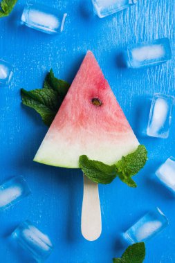 Hafif ahşap sopa ile karpuz dondurma, nane yaprakları, mavi ahşap arka plan buz küpleri. Dikey yönlendirme, düz yatıyordu, en iyi görünümü.