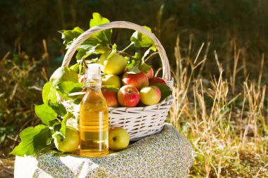 Yeşil ve kırmızı elma, elma suyu, meyve suyu veya cam şişe, sirke ile beyaz hasır sepet doğa arka planda, güneş ışığı bırakır. Yaz, sonbahar, taze elma hasat, hasat.