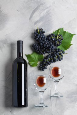 Şişe, iki kadeh şarap, üzüm yaprakları gri beton zemin üzerine ile. Kavram şarap üzüm, marka veya sommelier reklamlar. Dikey yönlendirme, üstten görünüm, düz yatıyordu.