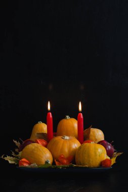 Cadılar Bayramı, Şükran günü, kabak, elma, kuru yapraklar, physalis, koyu arka plan üzerinde kırmızı mumlar ile sonbahar natürmort kompozisyon. Tablo dekorasyon konsepti, dikey yönlendirmesi, kopya alanı.