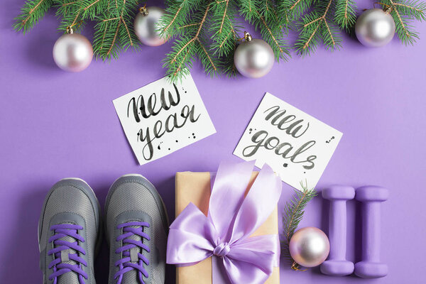Рождественская спортивная квартира лежала композиция серые ботинки фиолетовые гантели ремесла подарочная коробка с лиловым луком ели ветви буквы на фиолетовом фоне. Концепция новых целей на Новый год. Горизонтальный вид сверху
.