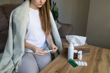 Evdeki vücut ısısını ölçmek için battaniyeye sarılı hasta kadın. Soğuk algınlığı, grip, kişisel bakım ve evde tedavi kavramı.