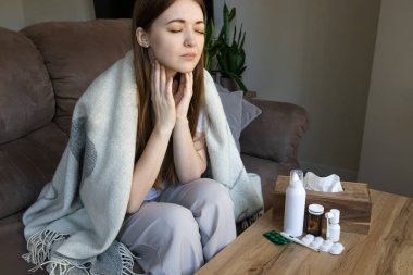 Battaniyeli hasta kadın boğazını tutuyor. Acı çekiyor ve yutkunmakta zorlanıyor. Grip, anjin, viral enfeksiyon ve evde sağlık hizmetleri kavramı.