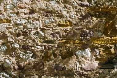 Düzensiz taş ve harç ile inşa edilmiş, kaba doku ve kırsal detayları gösteren, arka plan, tasarım projeleri veya mimari referanslar için mükemmel olan eski bir taş duvarın yakın çekimi.