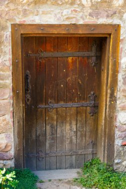 Eski bir taş duvarla çerçevelenmiş demir menteşeleri ve sapı olan sağlam bir ortaçağ ahşap kapısı. Köy girişi kale mimarisi ve tarihi işçiliği yansıtıyor..