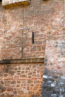 Dar bir yarık penceresi gösteren eski bir ortaçağ kale duvarının yakın çekimi. Kalıplı taş ve tuğla ustalığı, tarihi savunma mimarisini ve eski zanaatkarlığı gözler önüne seriyor..