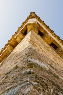 Dokulu ortaçağ duvarları olan tarihi bir taş kale kulesine yakın çekim. Fotoğraf, açık mavi gökyüzüne karşı mimari ve perspektifi vurguluyor.