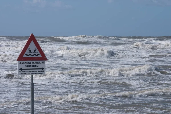 A sign warns for the risk of drowning by dangerous currents caused by a dam in the sea