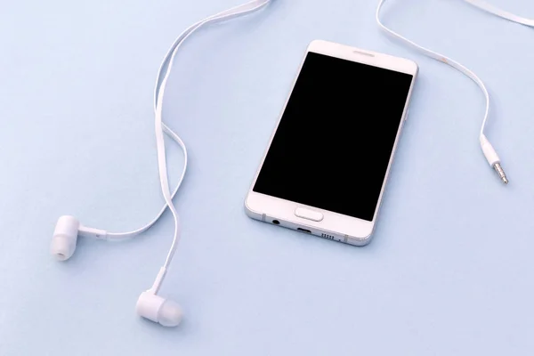 White smartphone and white headphones on blue background.