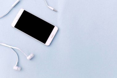 Beyaz smartphone ve mavi zemin üzerine beyaz kulaklık. Metin için yer.