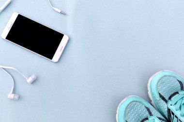 Beyaz smartphone, kulaklık ve spor ayakkabı mavi arka plan üzerinde çalışan turkuaz. Metin için yer.