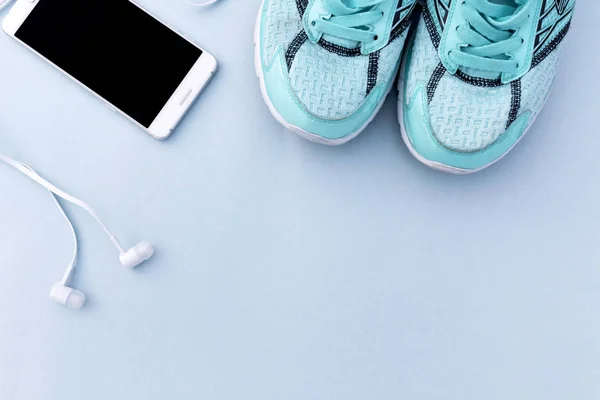 Beyaz smartphone, kulaklık ve spor ayakkabı mavi arka plan üzerinde çalışan turkuaz. Metin için yer.