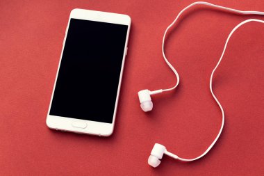 Beyaz smartphone ve kırmızı zemin üzerine beyaz kulaklık. Metin için yer.