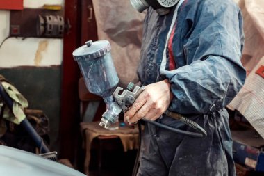 Koruyucu giysi ve sprey Kompresör kullanarak maske resim araba olan adam. Seçici odak üstünde el.