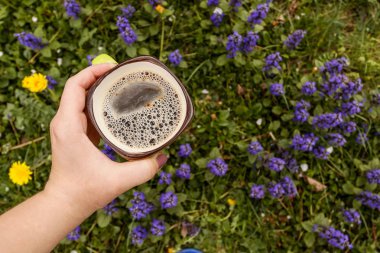 Kadın eli çiçekte bir fincan kahve. Açık havada. Metin için yer.