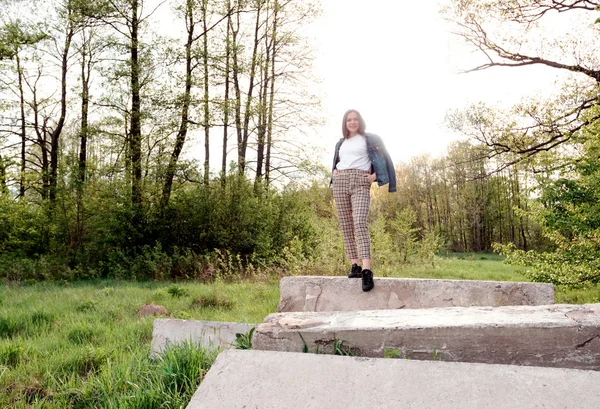 Mladá dívka s dlouhými hnědými vlasy stojící na skále v zeleném létě, jarní les. Místo pro text. — Stock fotografie