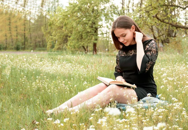 Girl reading book in garden, meadow of wild flowers. Concept of relaxation, recreation, self-development. Place for text.