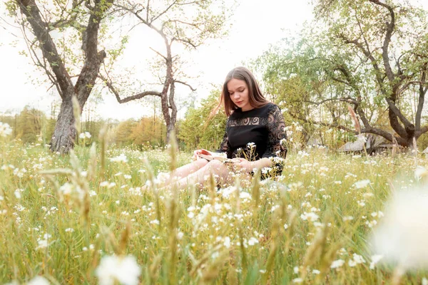 Dívka, která čte knihu na zahradě, louka divokých květin. Pojem relaxace, rekreace, self-development. — Stock fotografie