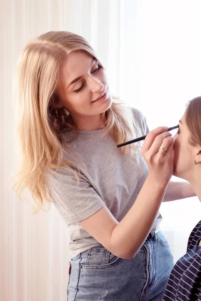 Make-up umělec dělá večerní make-up mladé dívky hnědé vlasy. Koncept krásy, péče o pleť, make-up. — Stock fotografie