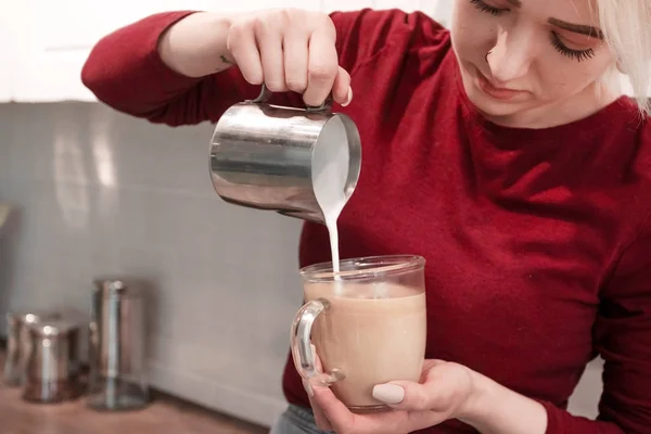 Kahve sanatı, kahve hazırlamak için elinde süt tutan genç ve güzel bir kız. Mutfakta kahve hazırlayan kız..