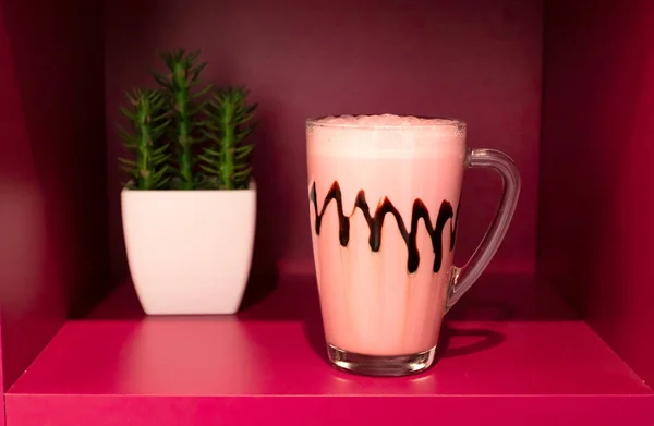 Cold pink milkshake in glass mug on pink background. Minimalism.