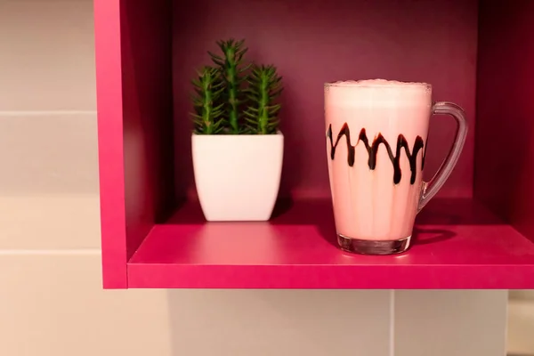 Cold pink milkshake in glass mug on pink background. Minimalism.