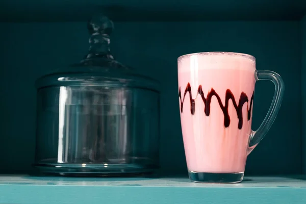 Cold pink milkshake in glass mug on blue background. Minimalism.