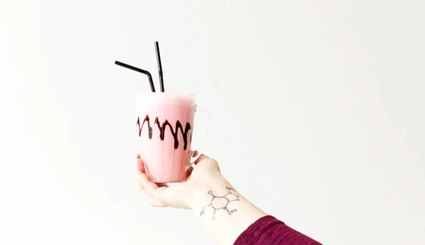 Studený růžový koktejl ve skleněném hrnku. Koktejl drží ženskou tetovací ruku. Minimalismus. Místo pro text. — Stock fotografie