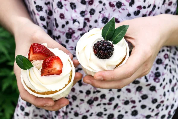 Girl holds in hands cupcakes with whipped cream and strawberries and blackberry. Festive party cakes for birthday, wedding.