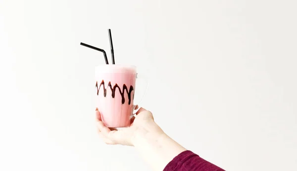 Cold pink milkshake in glass mug on. Cocktail holds female hand. Minimalism.