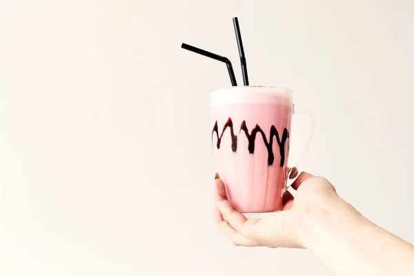 Cold pink milkshake in glass mug on. Cocktail holds female hand. Minimalism.