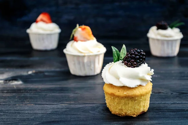 Cupcakes com chantilly e morangos e amoras no fundo azul velho. Bolos festivos de festa de aniversário, casamento . — Fotografia de Stock