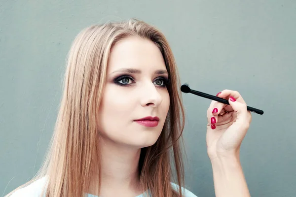 Schöne junge Mädchen mit professionellem Make-up auf grauem Hintergrund. Maskenbildnerin macht Augen-Make-up. — Stockfoto