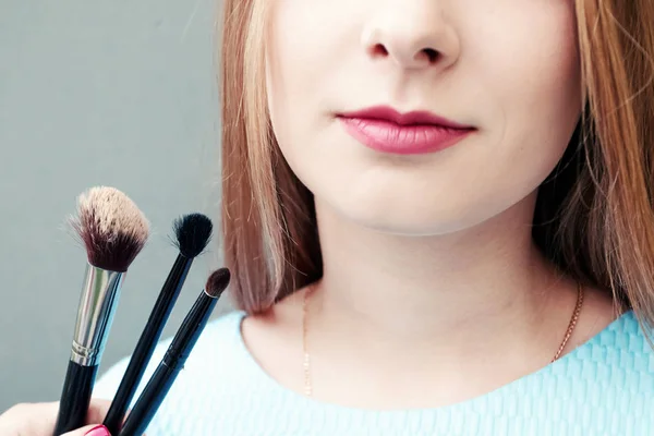 Krásná mladá dívka s profesionální make-up a make-up štětce na šedém pozadí. Koncept vzhazhist, móda, kosmetologie. — Stock fotografie
