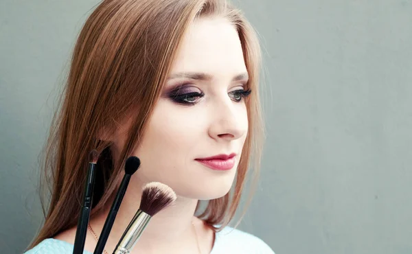 Schöne junge Mädchen mit professionellem Make-up und Make-up-Pinsel auf grauem Hintergrund. Konzept vzhazhist, Mode, Kosmetologie. Platz für Text. — Stockfoto